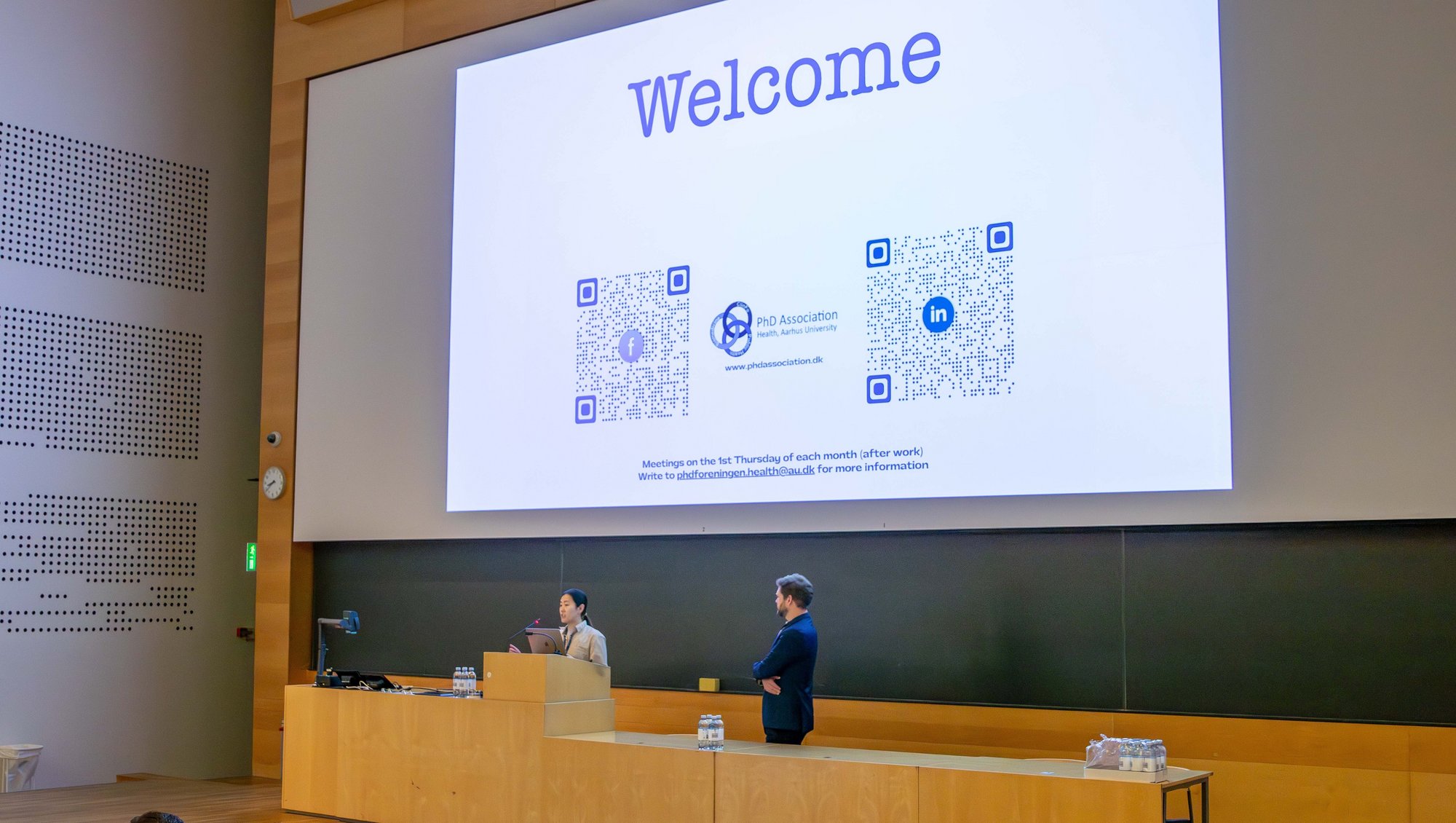 Med en varm velkomst i Per Kirkeby-Auditoriet blev PhD Day 2025 officielt skudt i gang af Anders Etzerodt, forperson for PhD Day 2025 og lektor på Institut for Biomedicin, samt Livie Yumeng Li, ph.d.-studerende og forperson for PhD-foreningen på Health. Foto: Simon Fischel, Health kommunikation.